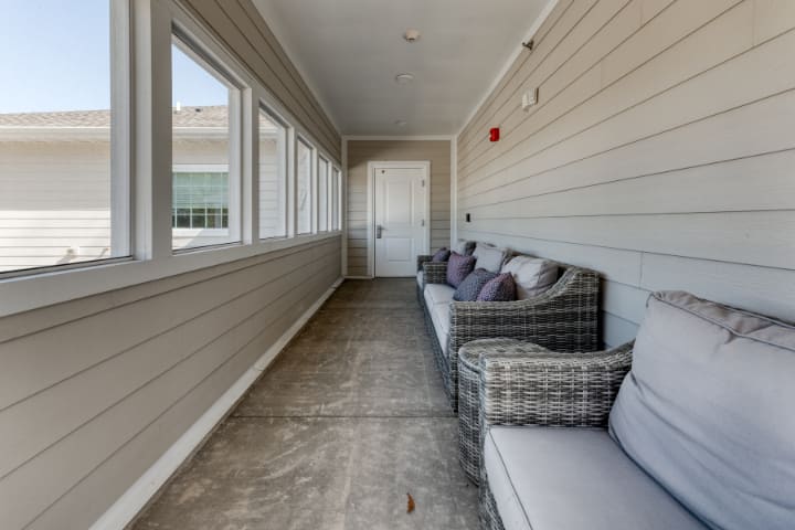 A cozy hallway with wicker sofas and cushions lining one side, facing large windows.
