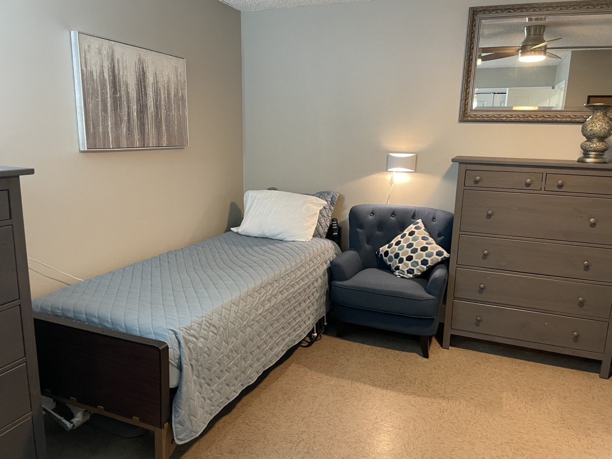 A cozy bedroom with a single bed, blue armchair, and a dresser.