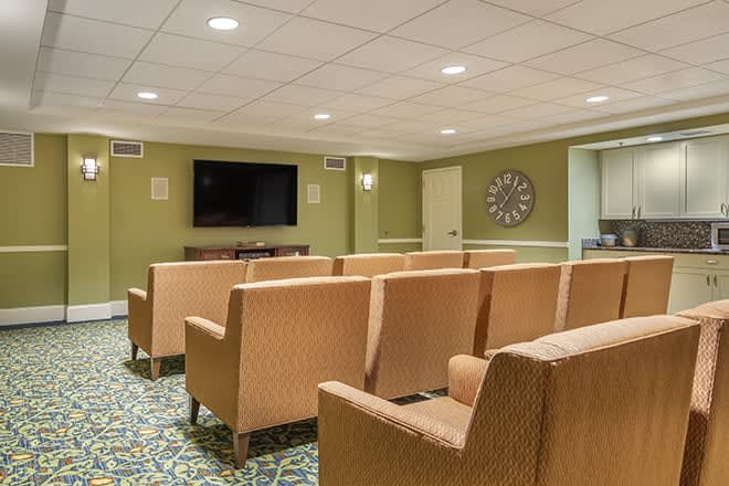 A cozy theater room with multiple rows of seating and a large television on the wall.