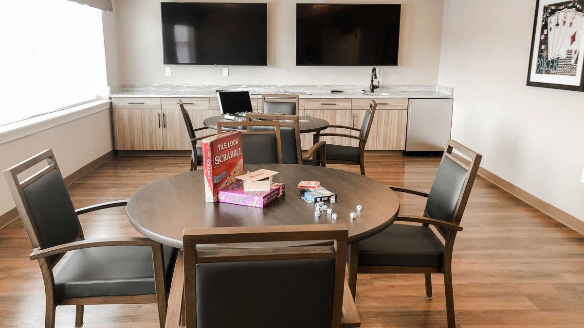 A modern conference room with a table and chairs, featuring board games, a laptop, and dual television screens.