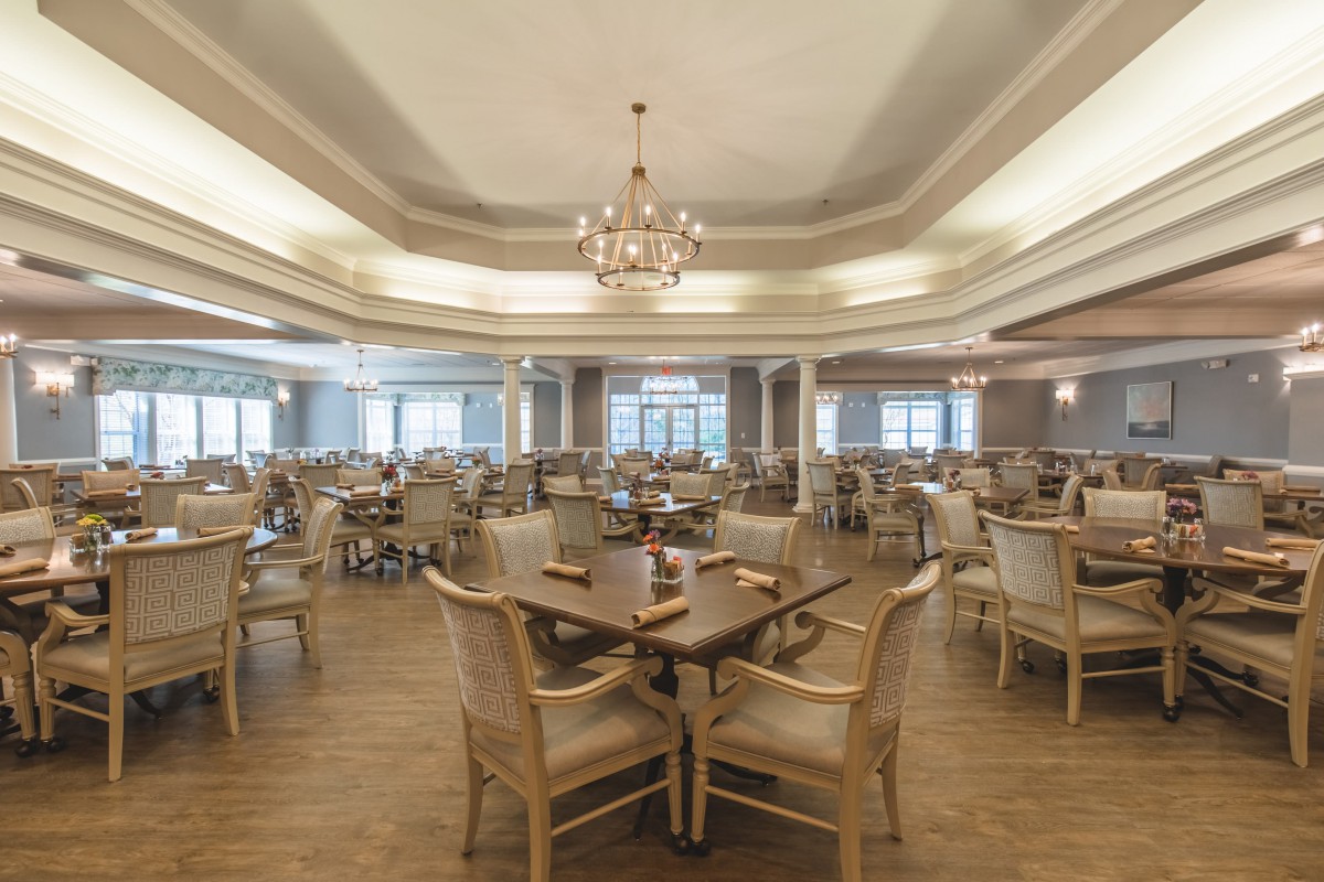An elegant dining room with neatly arranged tables and chairs, illuminated by a chandelier.