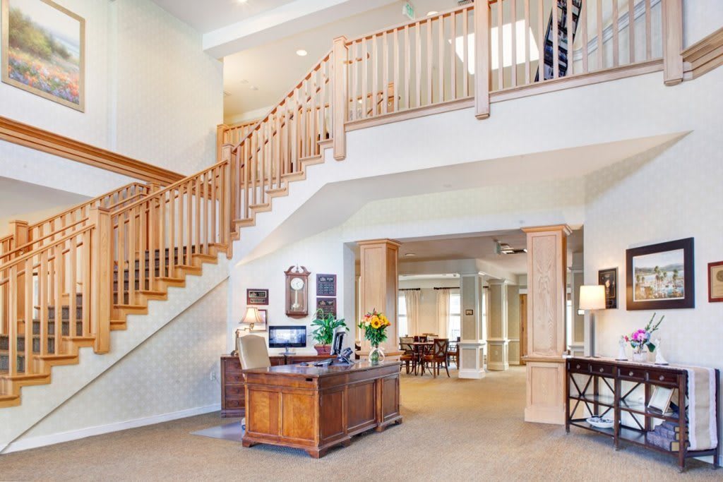 A spacious and well-lit lobby area with a wooden staircase and reception desk.