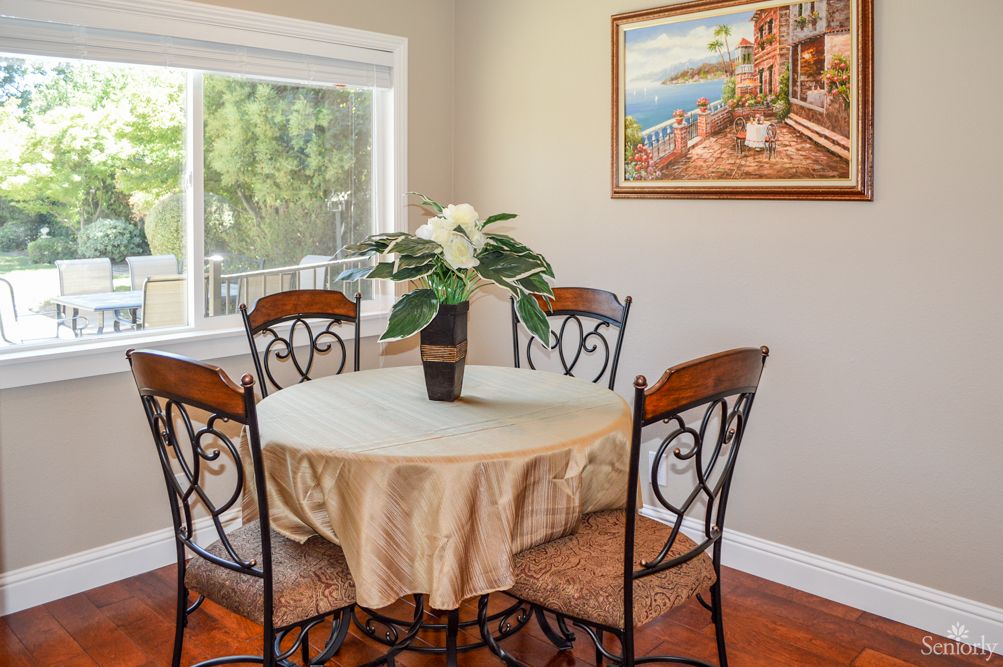 A cozy dining room with a round table, surrounded by four ornate chairs, a potted plant centerpiece, and a landscape painting on the wall.