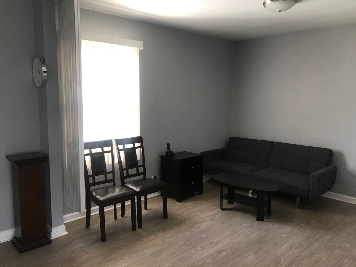 A minimalist living room with gray walls and wooden flooring, featuring a sofa, chairs, and a small table.