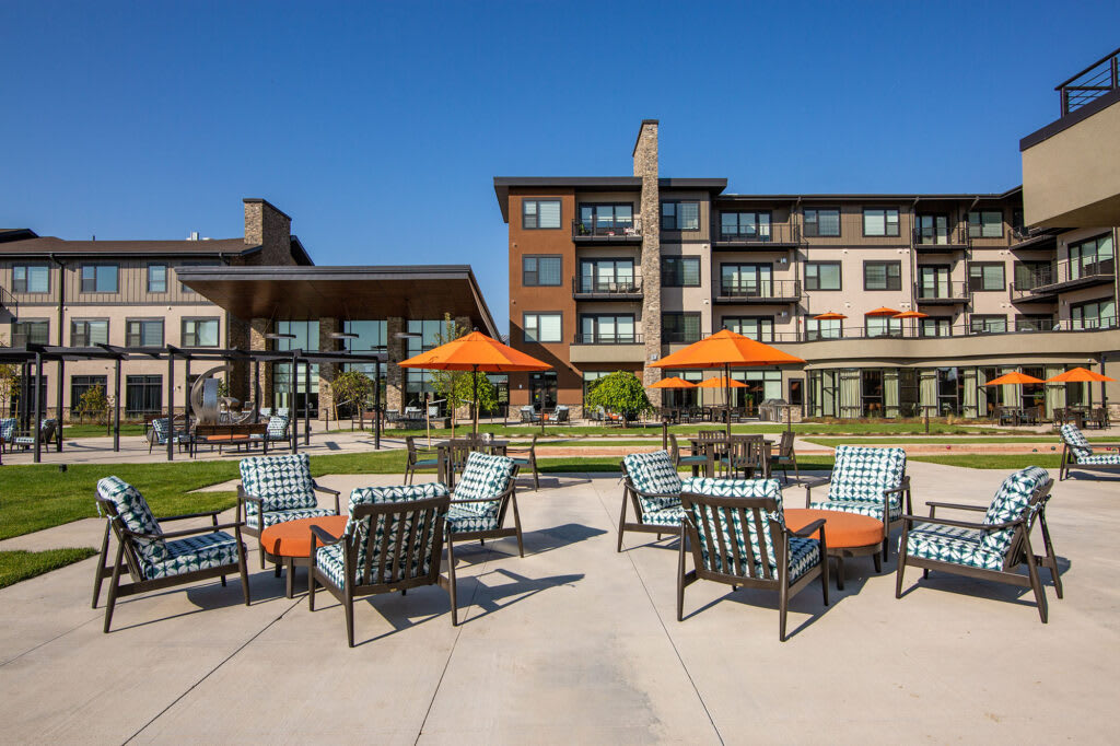 A modern outdoor patio area with seating and orange umbrellas in front of a multi-story building.