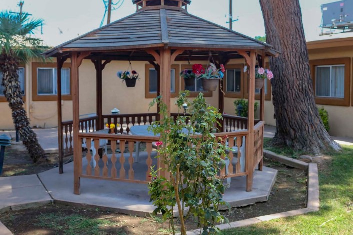 A wooden gazebo in a garden setting, surrounded by greenery.