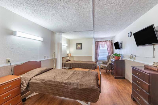 A spacious hospital room featuring two beds, a window with curtains, and essential furniture.