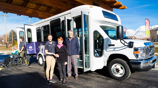 A group of three people stands in front of a new community bus, showcasing partnership and local transportation efforts.