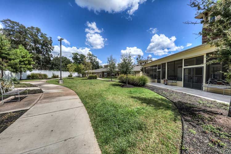 A scenic view of an outdoor area with a pathway, grassy lawn, and a modern building under a blue sky with clouds.