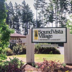 Entrance sign for Sound Vista Village, a retirement community surrounded by trees.