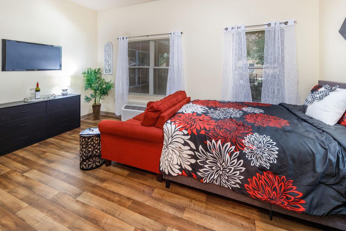 A cozy bedroom featuring a vibrant red sofa, floral-patterned bedding, and warm hardwood floors.