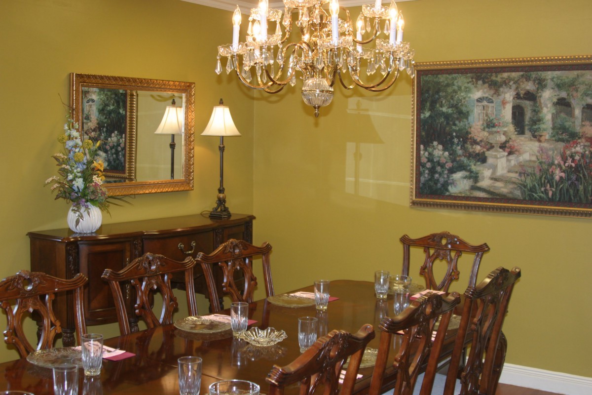 An elegant dining room featuring a chandelier, a long wooden table with chairs, and decorative artwork on the walls.