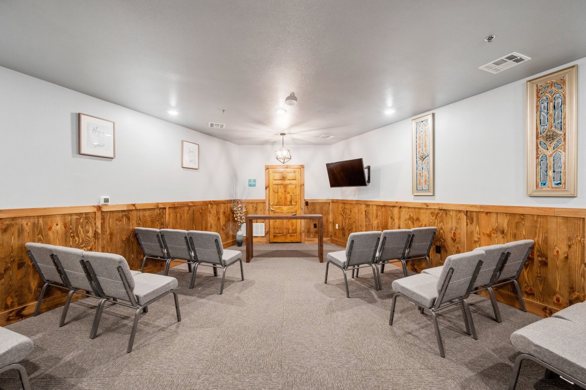 A small meeting room with chairs arranged in rows, featuring wood paneling and a mounted television.