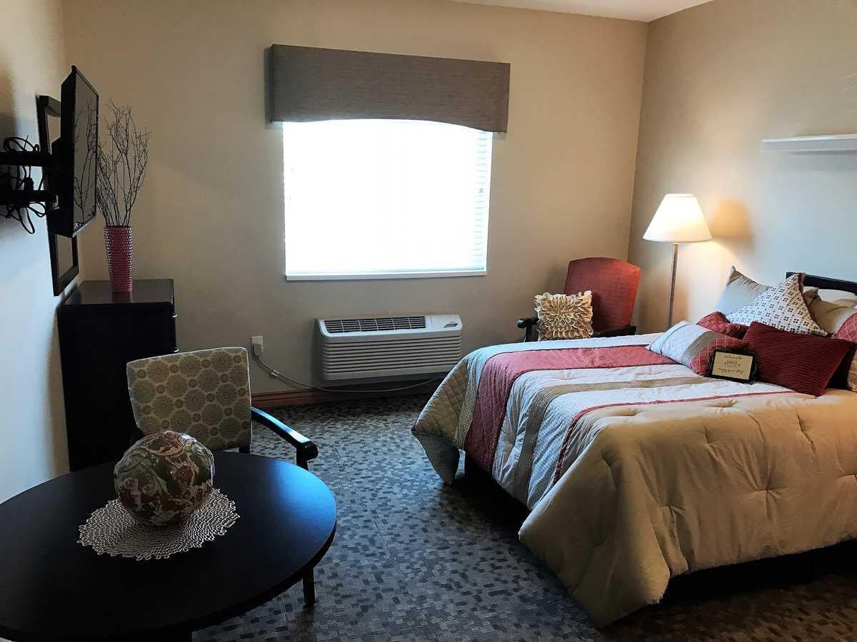 A cozy bedroom with a neatly made bed, a lamp, and seating area.