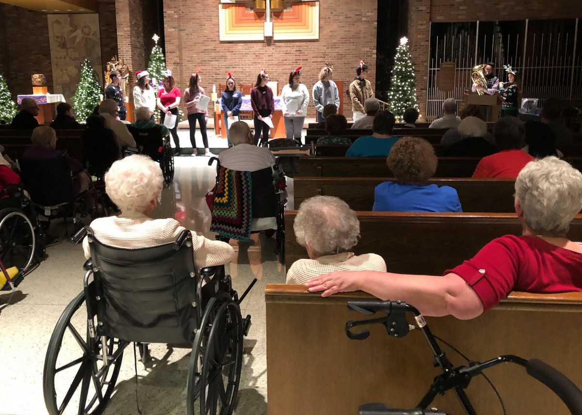 A group of people watching a performance in a church setting, with Christmas decorations.