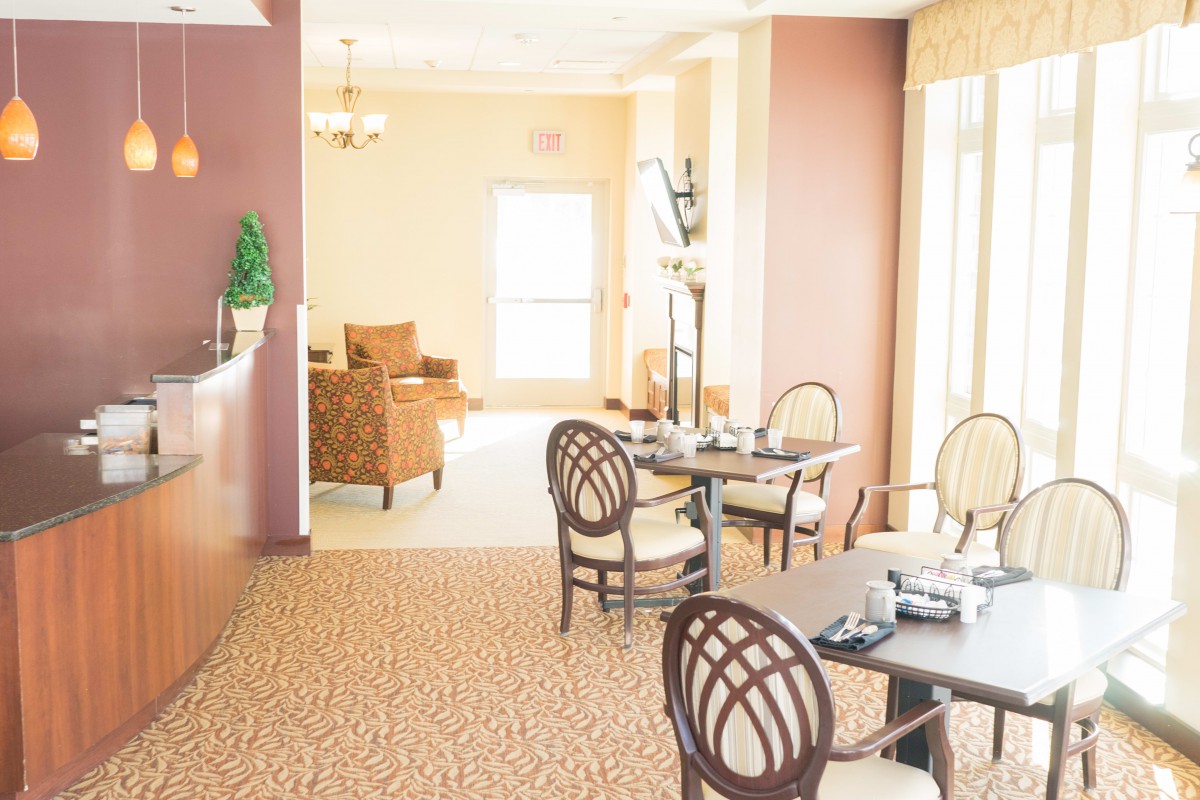A bright and elegant dining area with neatly arranged tables and chairs, featuring warm lighting and tasteful decor.