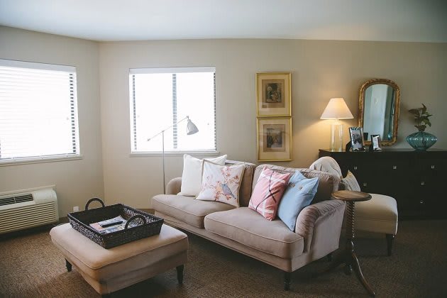 A cozy living room with a sofa, cushions, and a coffee table, warmly lit by a lamp.