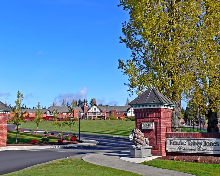 The entrance to a college campus with prominent signage, surrounded by green lawns and trees under a clear blue sky.