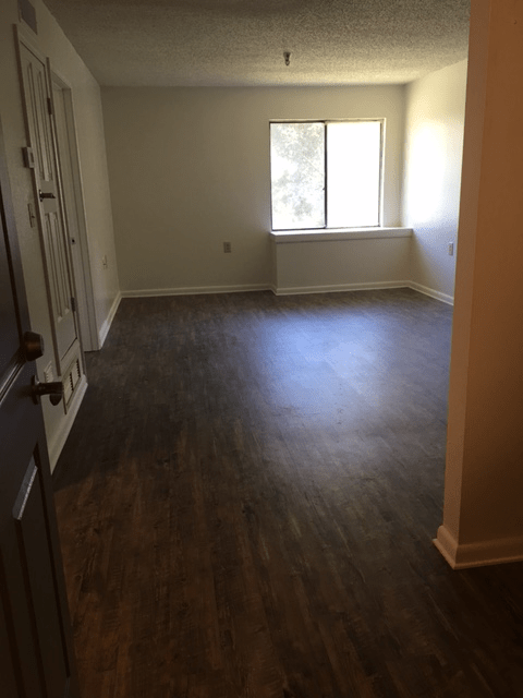 An empty room with hardwood flooring and a window letting in natural light.