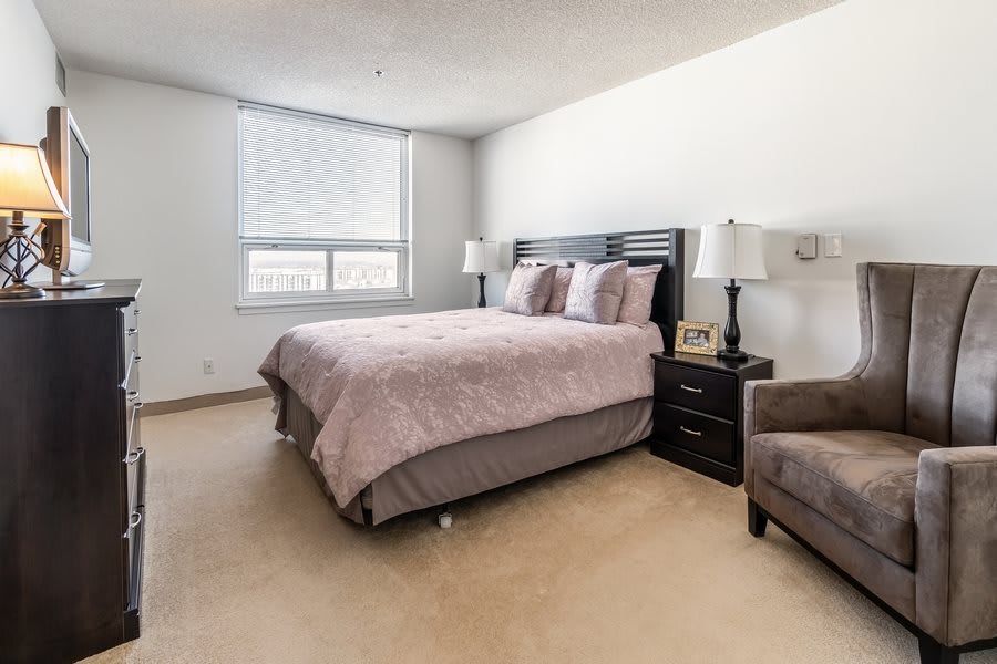 A cozy bedroom with a large bed, two nightstands with lamps, and a window letting in natural light.