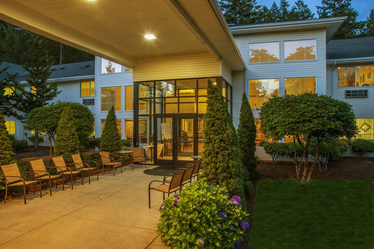 A well-lit hotel entrance with outdoor seating surrounded by manicured landscaping in the evening.