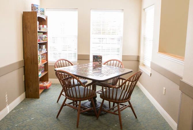 A cozy game room setup with a table, chairs, and a bookshelf by the window.