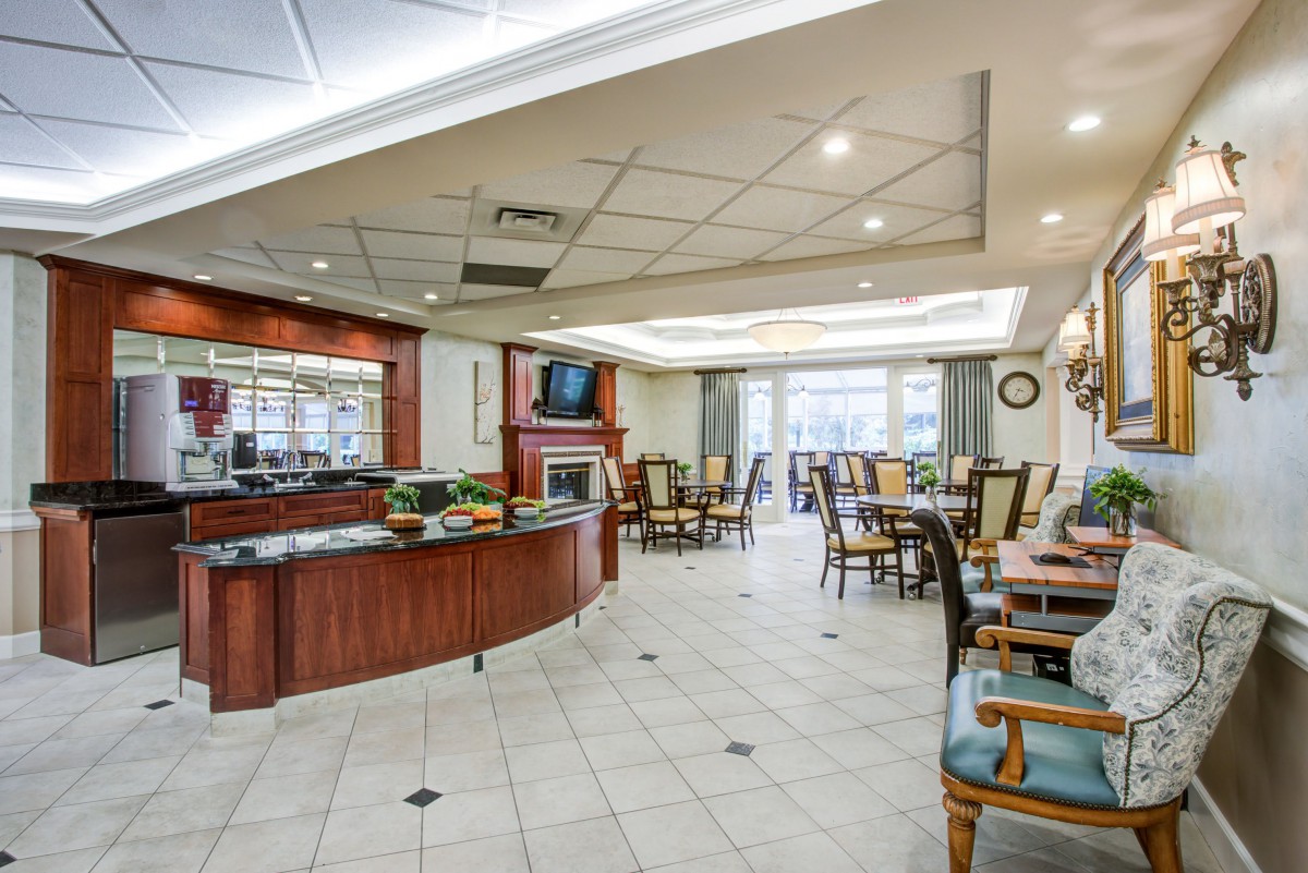 A modern dining area with a bar counter and multiple tables and chairs, well-lit by ceiling lights.