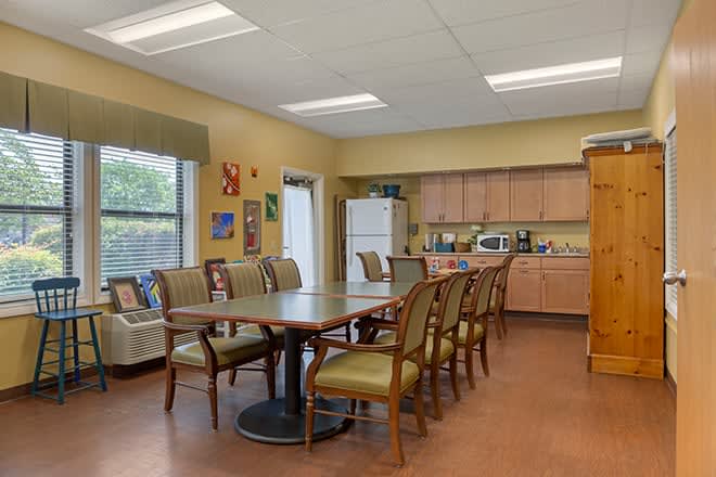 A cozy dining area with a large table and several chairs, featuring a kitchen setup with cabinets and a microwave.