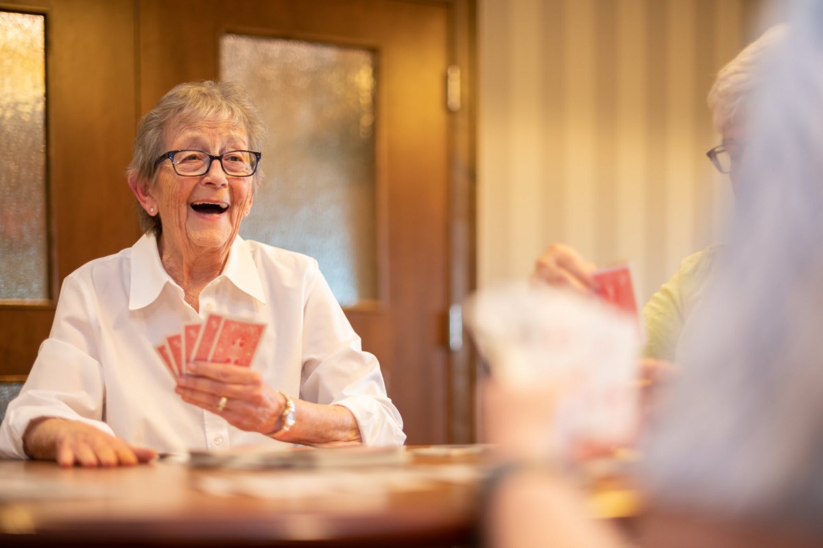 An elderly woman happily playing cards with friends.