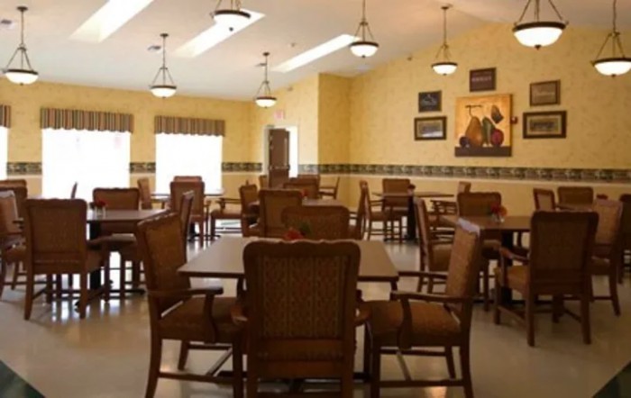 An empty dining room with wooden tables and chairs, warmly lit by ceiling fixtures.