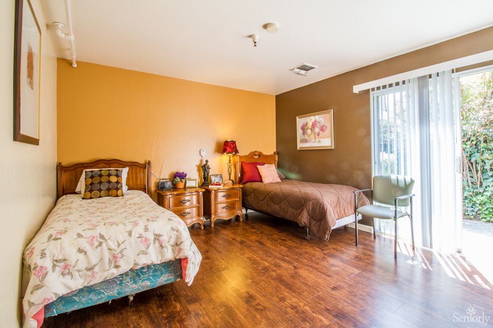 A cozy bedroom with two beds and wooden flooring, decorated with nightstands, lamps, and a window allowing natural light.