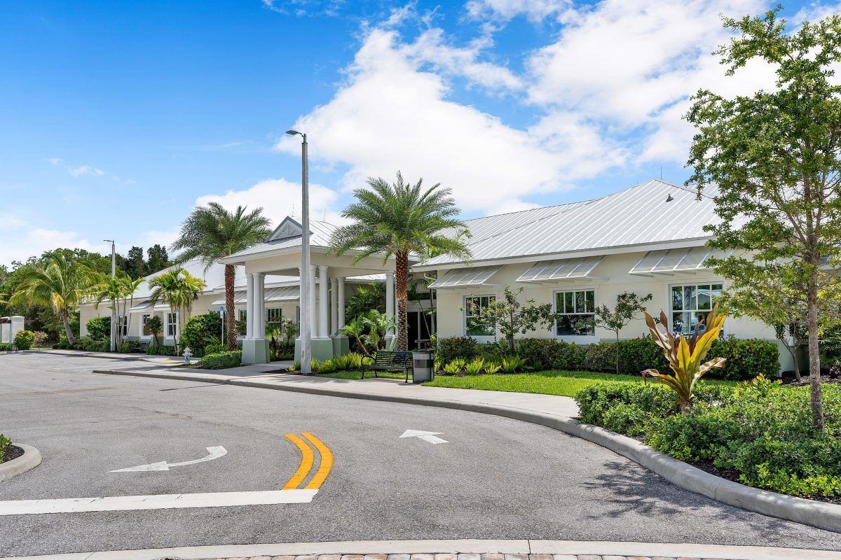 A modern building surrounded by palm trees with a curved road leading up to it under a partly cloudy sky.