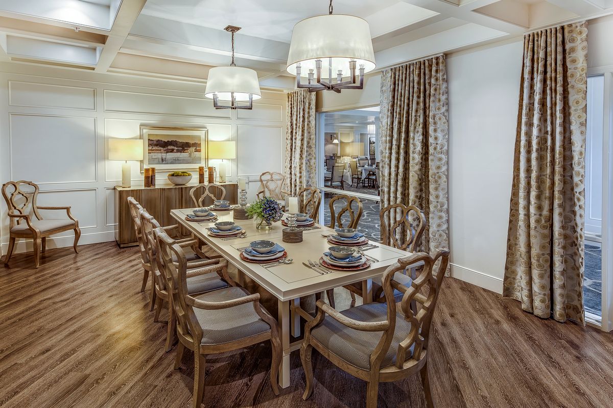 Elegant dining room with a long wooden table, set for a formal meal, featuring stylish chandeliers and warm wooden flooring.