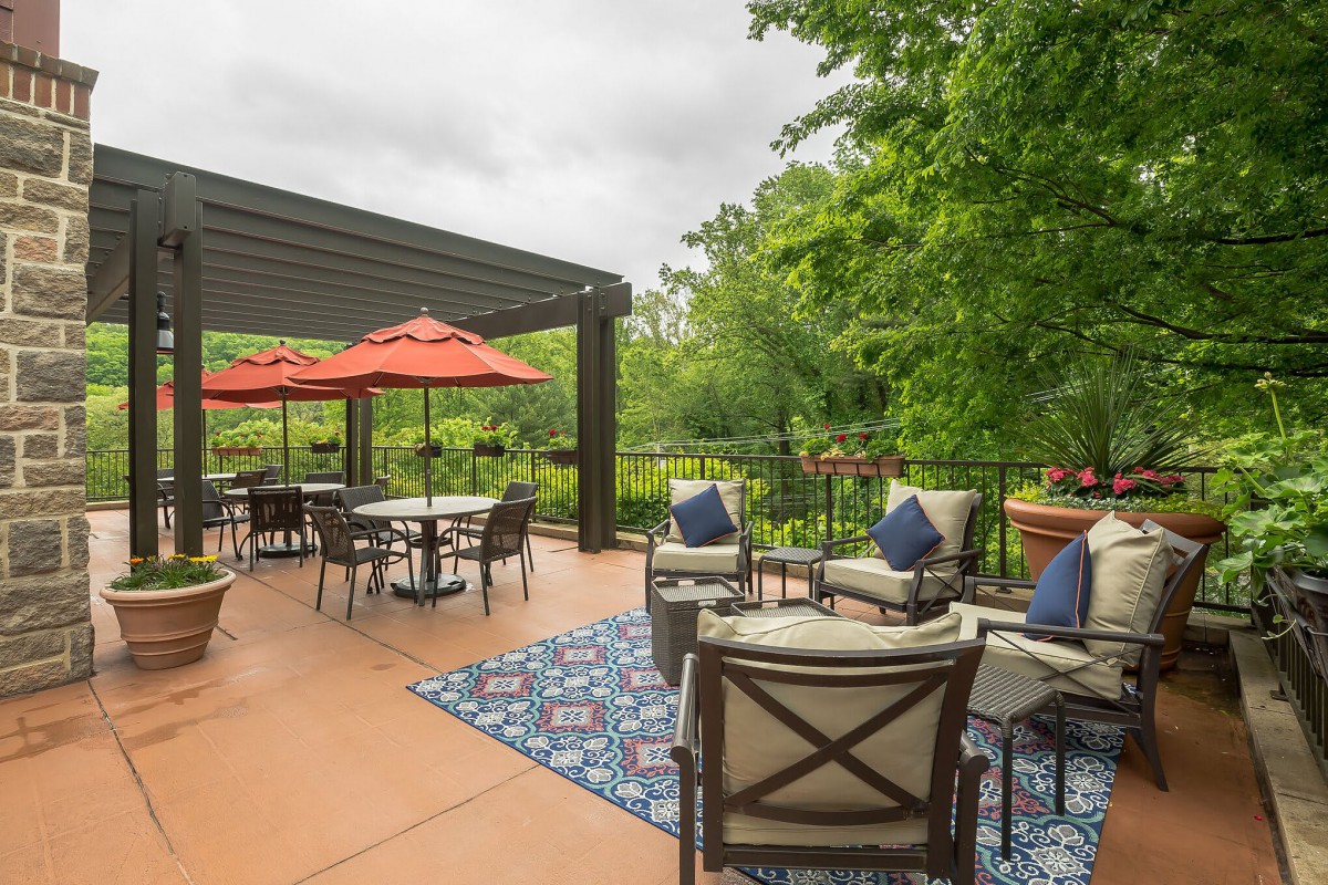 A spacious outdoor patio featuring comfortable furniture and red umbrellas, surrounded by lush greenery.