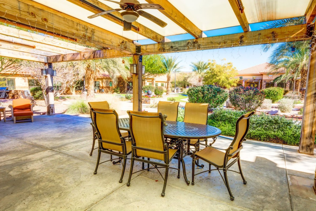 Outdoor patio area with a table and chairs under a pergola, overlooking a lush garden.