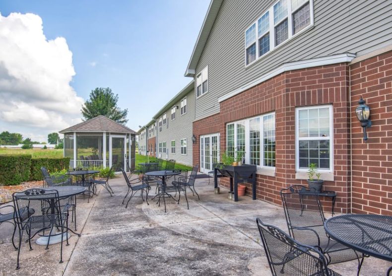 An outdoor patio area with tables and chairs next to a building, featuring a gazebo in the background.