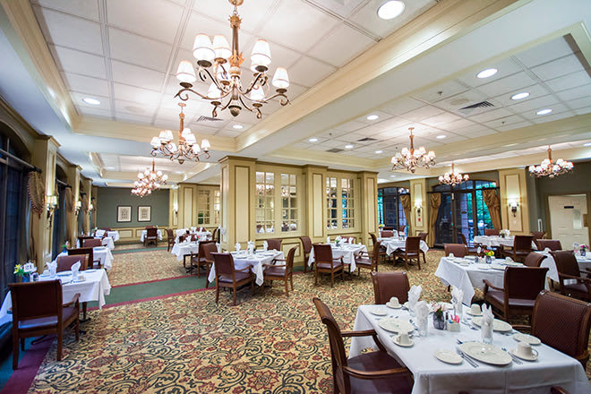 An elegant restaurant dining room with chandeliers and tables set with white tablecloths.