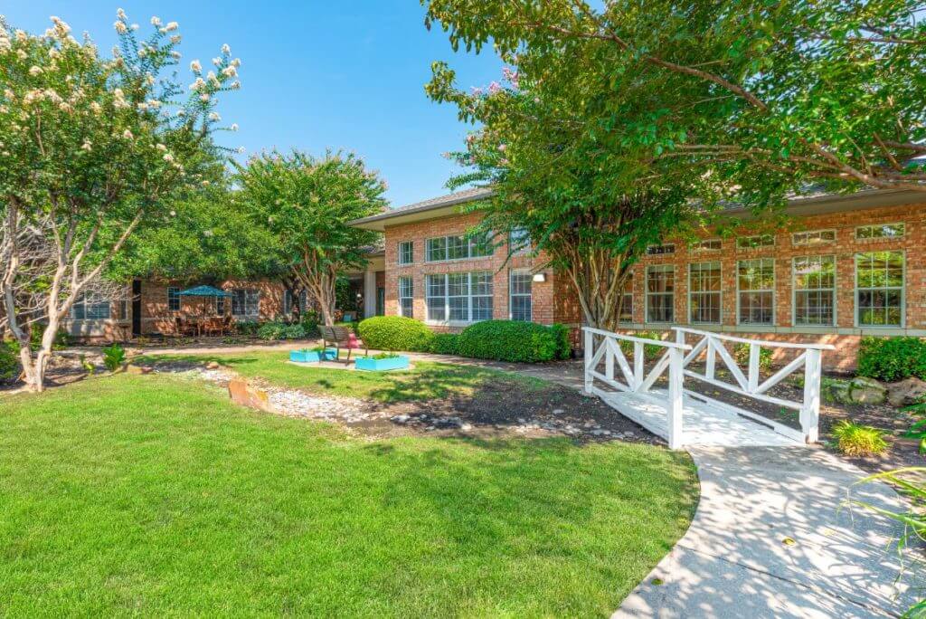 A scenic view of a building surrounded by a lush garden with trees and a well-maintained lawn.