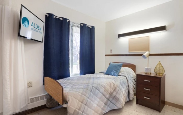 A cozy bedroom with a single bed, blue curtains, and a small dresser.
