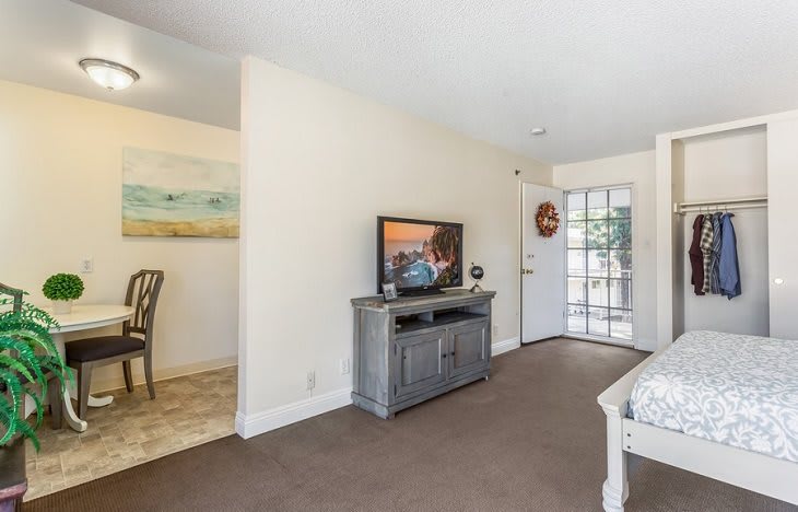 A cozy living room with a television and modern furniture, featuring a view of the adjacent dining area.