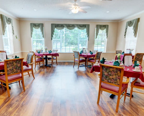 A brightly lit dining room with wooden chairs and tables set near large windows.