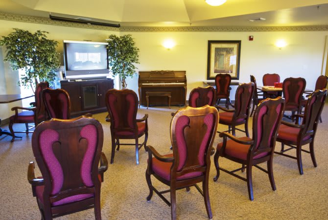 A small meeting room with arranged chairs facing a television and a piano.