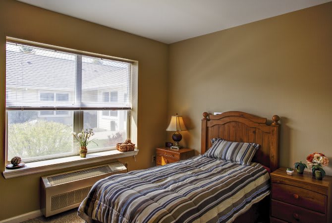 A cozy bedroom with a single bed, striped bedding, and a nightstand beside a large window.