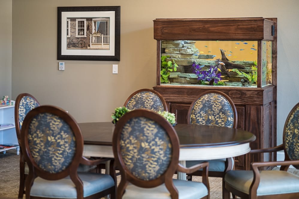 A cozy dining room featuring a round table with floral upholstered chairs, complemented by a large fish tank and wall art.