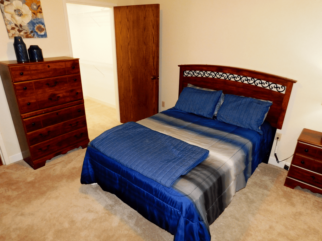A cozy bedroom with a neatly made bed featuring blue bedding and a wooden dresser.