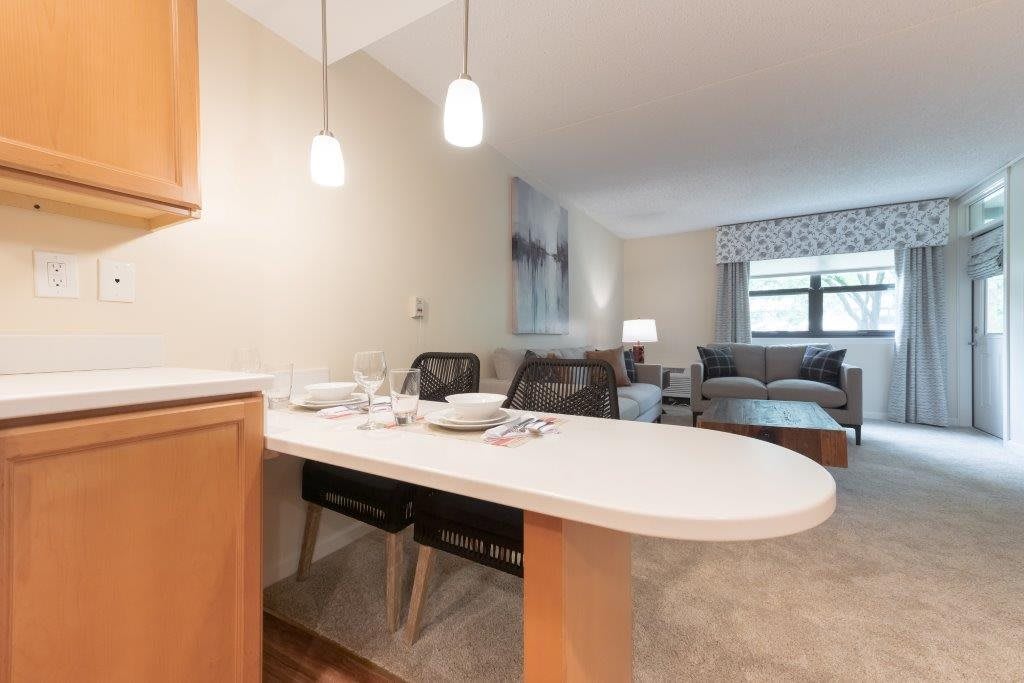 A cozy living room with a connected dining area featuring a table and chairs, pendant lighting, and a comfortable sofa near the window.