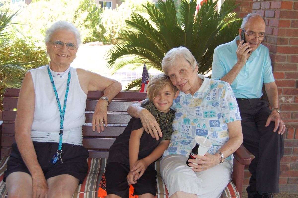 A family group enjoying a sunny day outdoors, sitting on a bench.