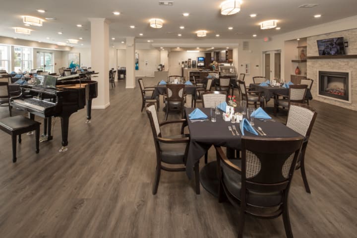 A spacious restaurant interior with elegantly set tables and a piano.