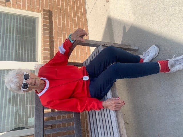 A person wearing a red sweater and sunglasses sits casually on a bench outdoors.