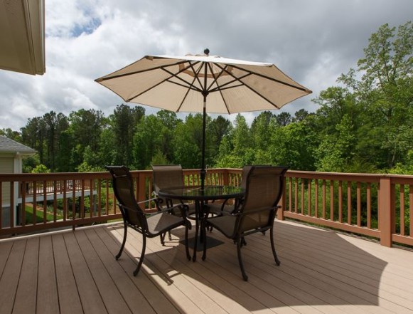 A patio set with an umbrella on a wooden deck overlooking a lush green landscape.